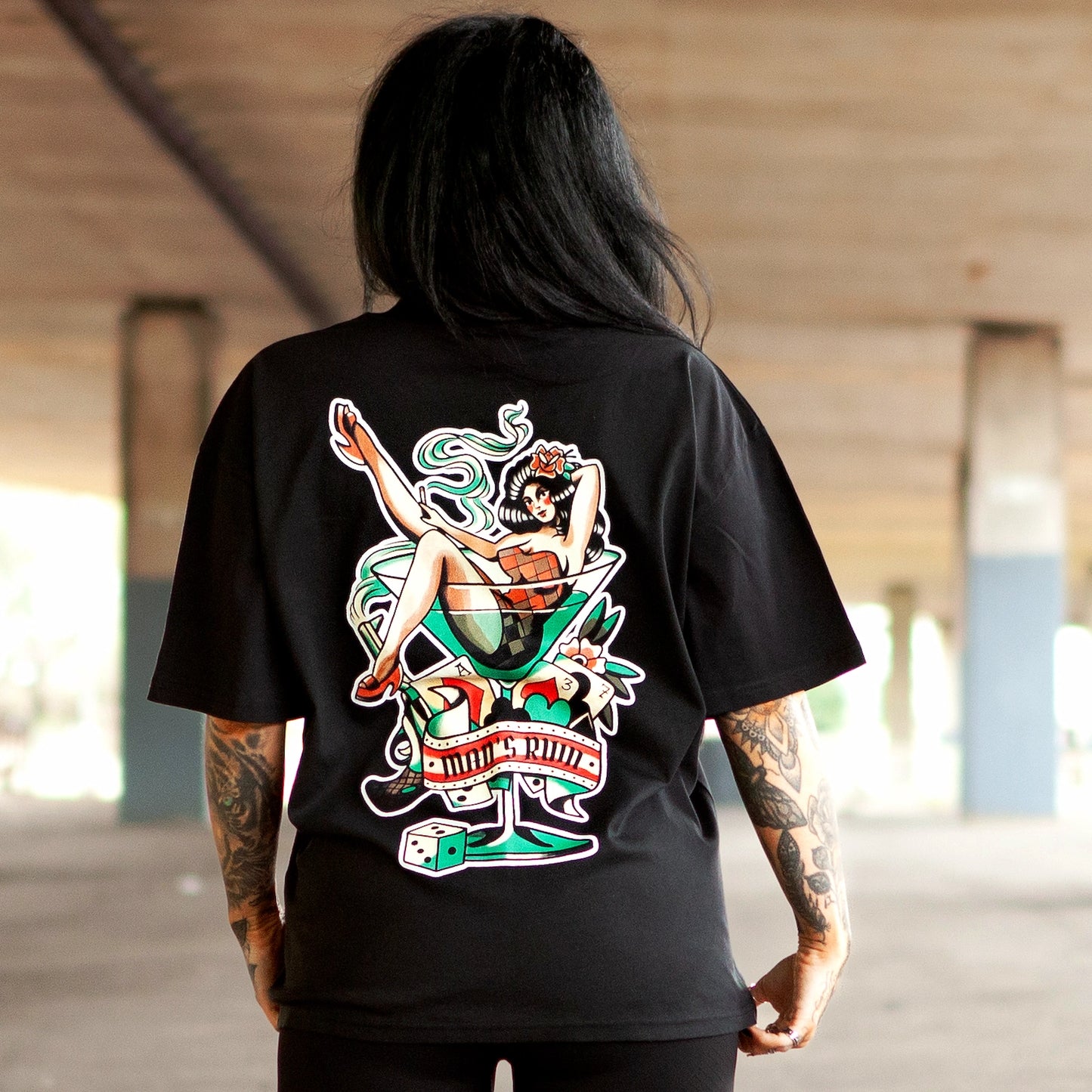 Model wearing Haunt’s Man’s Ruin oversized black t-shirt featuring a bold pin-up girl in a martini glass back print, captured under an overpass in Bristol.