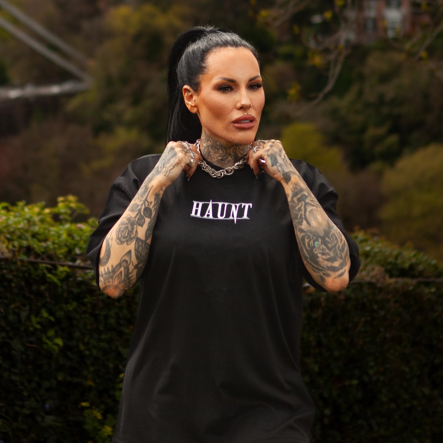 Front view of the Softcore Bloom premium t-shirt with HAUNT logo, worn by tattooed model standing in front of Bristol’s Clifton Suspension Bridge.
