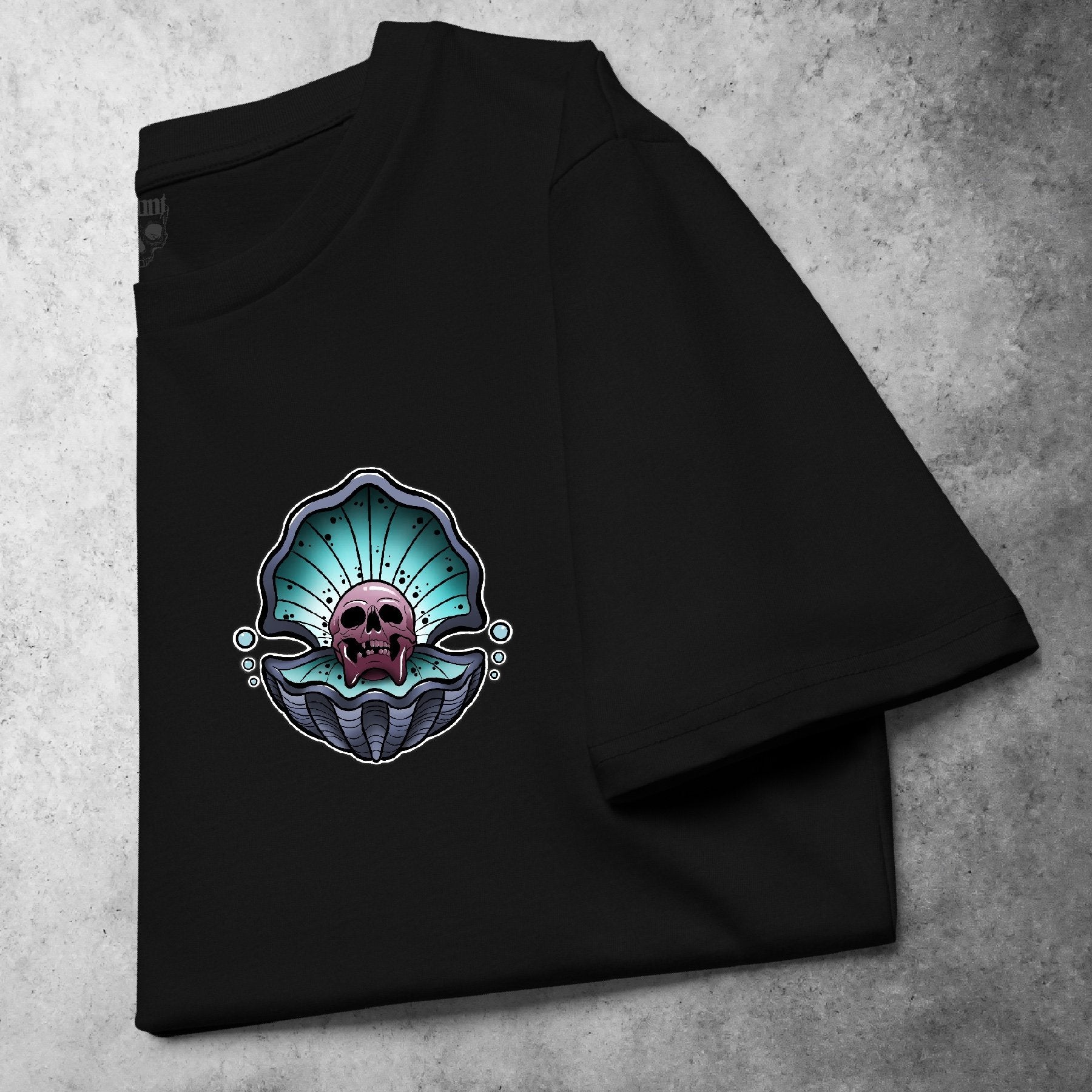 Cursed Pearl Pocket Tee in black, featuring a bold skull within an oyster shell design. Tattoo-inspired graphic with gritty detailing, presented on a folded heavyweight t-shirt.