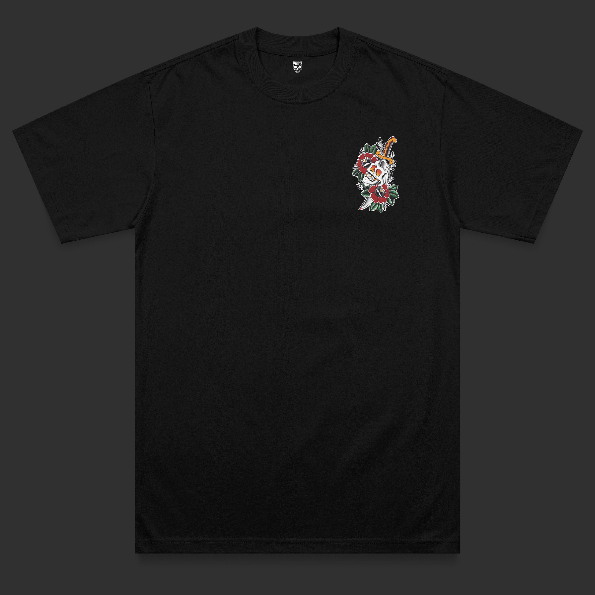 Front view of the Last Laugh heavyweight t-shirt featuring a traditional tattoo-inspired skull and dagger chest print surrounded by red flowers and green leaves on a black heavyweight garment.