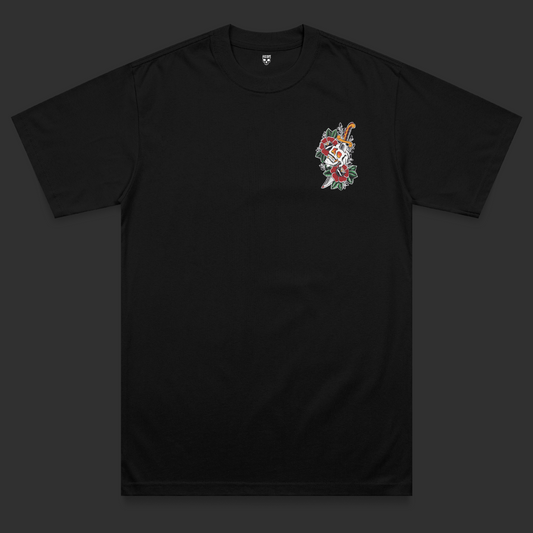 Front view of the Last Laugh heavyweight t-shirt featuring a traditional tattoo-inspired skull and dagger chest print surrounded by red flowers and green leaves on a black heavyweight garment.