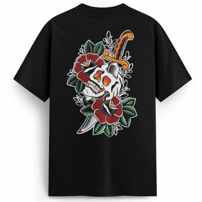 Black premium oversized t-shirt with a bold back print featuring a skull split by a dagger, surrounded by deep red traditional roses and green leaves. Classic tattoo-style design with high contrast and vibrant detail.