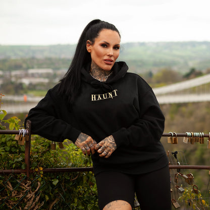 Model wearing the Until Death hoodie, front view showing gold HAUNT logo at Bristol observatory with scenic background.